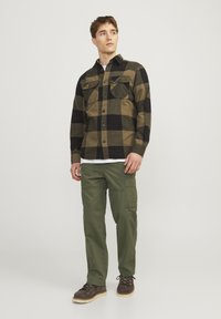 Sort og olivengrønternet flannel skjorte, to brystlommer, kombineret med olivengrønne cargo bukser og brune støvler.