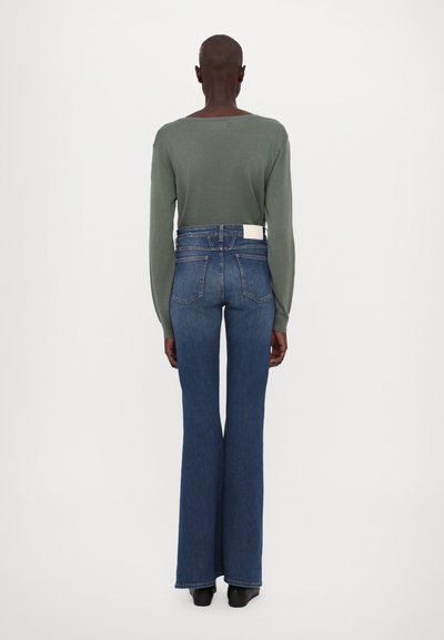 Blusa verde de manga larga combinada con jeans acampanados azules. Los jeans tienen una cintura alta, detalles de bolsillo de parche y una textura de tela ligera.