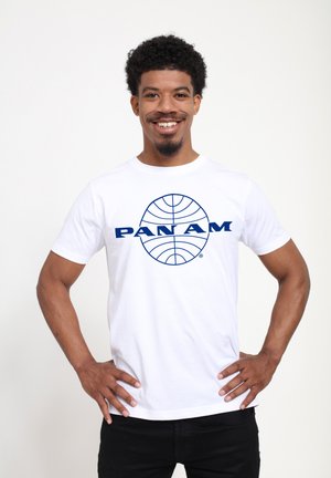 T-shirt en coton blanc avec un grand logo bleu "PAN AM" et un motif de globe sur le devant. Manches courtes, col ras du cou et coupe décontractée.