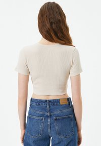 Beige, gekruiste rib T-shirt met korte mouwen, voorzien van een ronde halslijn en een textuurstof. Draagt met hoge taille, blauwe jeans.