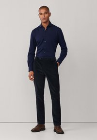 Marineblauwe blouse met verspreide kraag, gecombineerd met zwarte ribfluwelen broek en bruine geklede schoenen, wat een formele uitstraling creëert.