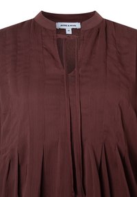 Braune Bluse mit einem kragenlosen Design, vertikaler Textur und einem Schlüsselaufriss. Verfügt über Falten am Saum und ein Markenetikett innen.