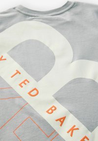 Grå bomulds t-shirt med store lysegrå bogstaver og grafisk design. Har orange bogstaver og vinklede detaljer på et tekstureret stof.