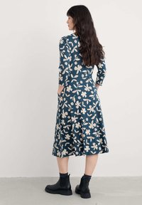 Sukienka do kolan o ciemnozielonym tle z białym kwiatowym wzorem. Posiada rękawy do trzech ćwiartek oraz boczne kieszenie, zestawiona z czarnymi botkami na kostkę.