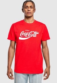 Červené bavlněné tričko s nápisem "Užijte si Coca-Colu" v bílé kurzívě přes hrudník. Krátké rukávy, kulatý výstřih a pohodlný střih.