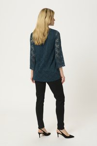 Top in pizzo teal con maniche a tre quarti e orlo scallop, abbinato a pantaloni neri aderenti e décolleté nere a punta.