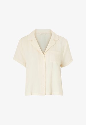 Camisa de manga corta de color crema hecha de tela ligera. Presenta un cuello con muesca, cierre de botones y un bolsillo en el pecho.