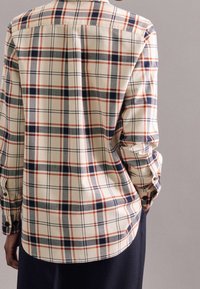 Camicia a maniche lunghe a quadri color crema, con quadrati blu navy, rossi e grigi. Caratterizzata da un orlo dritto e maniche con polsini abbottonati. Tessuto morbido e texture.