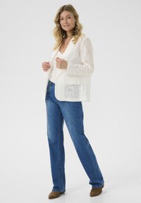 Lichtgewicht, geborduurde witte blazer met een semi-doorzichtige textuur, gecombineerd met blauwe rechte jeans en bruine schoenen.