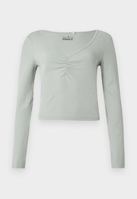 Μακρυμάνικη μπλούζα σε ανοιχτό πράσινο χρώμα, κατασκευασμένη από ριμπ ύφασμα, με V-λαιμόκοψη και πιετά λεπτομέρεια στο κέντρο μπροστά. Κοντό μήκος.