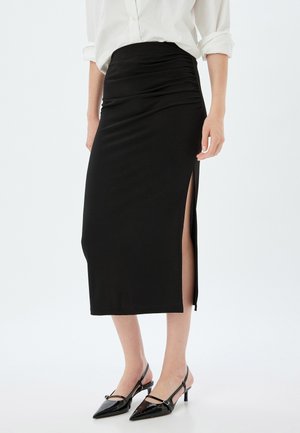 Black midi skirt with a high waistband, gathered texture, and a side slit, paired with black pointed-toe slingback heels.