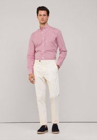 Rot-weiß gestreiftes Hemd mit Knöpfen, weiße Hose und schwarze Espadrilles. Einfaches Design, taillierte Passform, glatte Texturen und kontrastierende Farben.