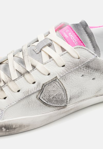 Silver leather sneaker with a textured finish, grey accents, and a bright pink tongue. Features a shield logo and white laces.