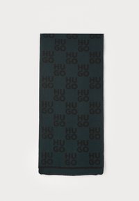 Sort tørklæde med gentagende "HUGO" logo mønster på en mørkegrøn baggrund. Materialet virker blødt med en frynset kant. Rektangulær form.