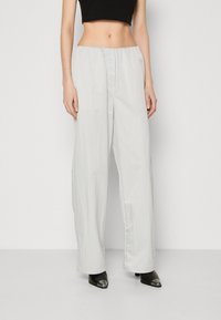 Pantalons larges gris clair fabriqués dans un tissu léger et lisse. Dotés d'une taille élastique et d'une coupe décontractée, associés à des chaussures noires à talons pointus.