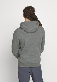 Felpa grigia con tessuto texture, dotata di cappuccio, polsini a costine e orlo. Il design è semplice, senza motivi o accenti prominenti.