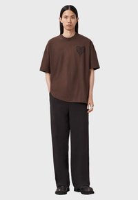 Brun oversized t-shirt med en sort hjertegrafik på venstre bryst, kombineret med sorte bukser med brede ben og sorte sko.