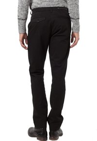 Černé kalhoty s úzkým střihem, vybavené zadními kapsami, plochým předním dílem a hladkou strukturou, v kombinaci s světle šedým svetrem a černými botami.