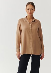 Beige satijnen shirt met knopen, met een kraag, lange mouwen en een relaxed fit. Heeft kleine knopen en een licht gebogen zoom.