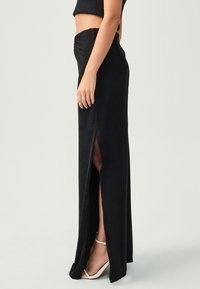 Melnā maksi svārki ar augstu šķēlumu, izgatavoti no mīksta auduma. Ar drapētu vidukli un elegantu, pieguļošu siluetu. Uzsvērti ar smalku gaismas atspīdumu.