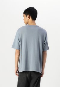 Camiseta de algodón azul claro con mangas cortas, cuello redondo y un corte relajado, mostrada desde atrás. Presenta un sutil detalle de costura.