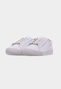 Paire de baskets blanches basses avec des lacets blancs et un détail de texte doré subtil sur le côté, sur un fond clair uni.