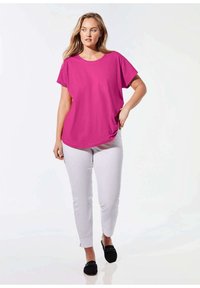 Fuchsia shirt met korte mouwen en een ronde hals, gecombineerd met lichtgrijze slim-fit broek en zwarte instapschoenen. Gladde stoftextuur.