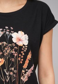 Svart bomull T-skjorte med blomsterdesign i pastellfarger, med korte rullede ermer og rund hals.