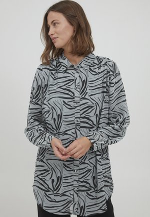 Chemise à manches longues avec boutons en gris clair, ornée d'un motif zebra noir. Elle dispose d'un col et de poignets froncés. Tissu doux et texturé.