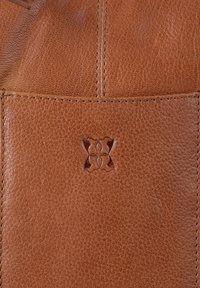 Brown leather bag featuring a textured surface, stitched accents, and a decorative embossed logo in the center.
