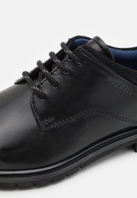 Chaussure noire en cuir à lacets avec col texturé, coutures détaillées et semelle épaisse en caoutchouc, vue rapprochée de côté et de dessus.