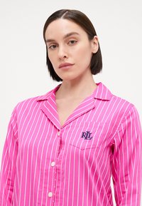 Parte superior de pijama a rayas rosas con cuello, cierre de botones y un bolsillo en el pecho izquierdo que presenta las letras "RL" bordadas en azul marino.