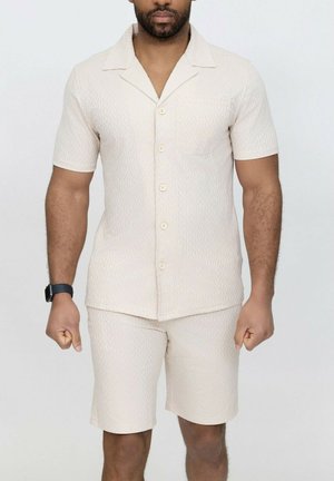 Chemise à manches courtes, à boutons, et shorts assortis en beige clair avec un motif en zigzag. Fabriqué en tissu texturé avec une poche sur la chemise.