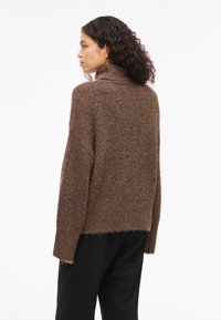 Pull en maille marron avec un col montant, une coupe ample, des épaules tombantes et un ourlet côtelé. Tissu texturé à l'apparence douce.