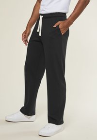 Black sweatpants with a drawstring waist, side pocket, and relaxed fit. Paired with white sneakers for a contrasting look.