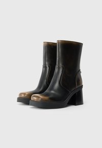 Bottines en cuir noir avec un accent dégradé marron, bout rond et talon épais. Le design présente des découpes sur les côtés.