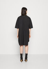 Czarna sukienka z krótkimi rękawami, z wysokim dekoltem, luźnym krojem i bocznymi rozcięciami. Gładki materiał o minimalistycznym wzornictwie.