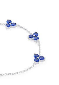 Silberne Armbanduhr mit vier runden blauen Steinen, die in einem floralen Muster angeordnet sind und durch eine filigrane Kette verbunden sind. Glatte Metalloberfläche.