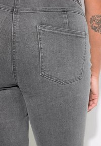 Jeans de mezclilla gris con una textura suave, que presentan un bolsillo trasero cosido y un diseño de pierna tapered. Hay un acabado sutil y uniforme.