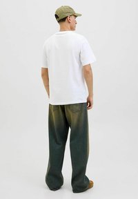 Camiseta de algodón blanca con un corte relajado, combinada con unos pantalones vaqueros verdes holgados que muestran un degradado de color y dos bolsillos traseros.
