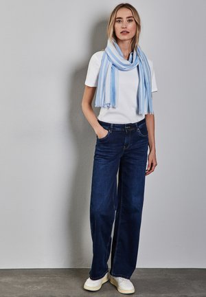 Weißes T-Shirt mit kurzen Ärmeln, dunkelblaue weite Jeans, hellblauer gestreifter Schal, getragen mit weißen Sneakers, vor einem neutralen Hintergrund stehend.