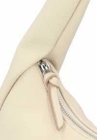 Angolo di borsa in pelle beige con superficie strutturata, dotata di una cerniera argentata e di un tirante in pelle, che mette in risalto linee pulite e curve morbide.