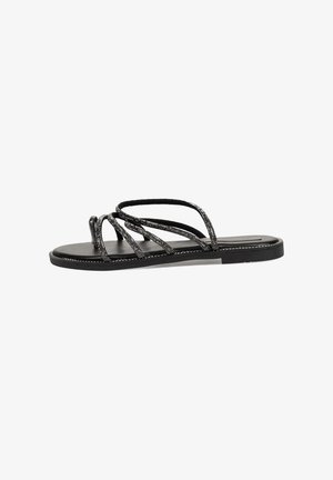 Sandalias planas negras con múltiples tiras entrelazadas, que presentan una textura brillante y una suela negra suave. Diseño minimalista para uso casual.