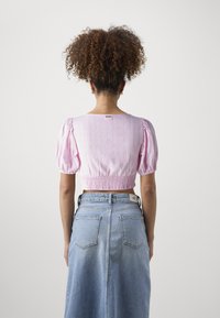 Rosa kort bluse med puffærmer og smocket kant, parret med en højløftet blå denimnederdel med lommeudskæringer.