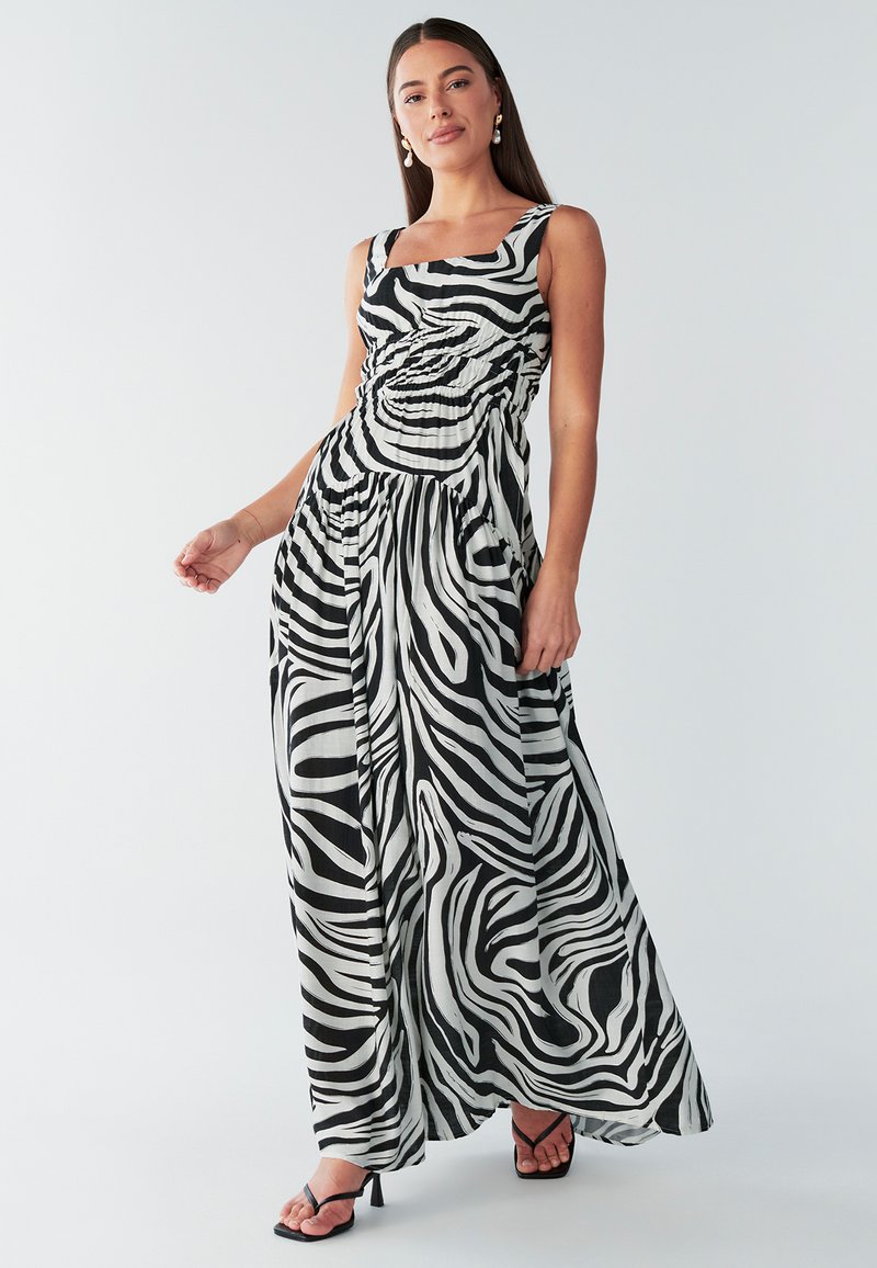Abito lungo con stampa zebre in bianco e nero. Scollo quadrato, corpetto aderente e gonna fluente con texture a pieghe. Abbinato a sandali neri con tacco.