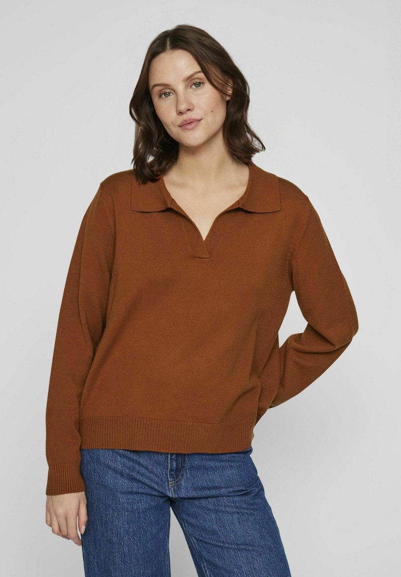 Suéter de punto marrón con escote en V y cuello, puños y dobladillo acanalados. Combinado con unos vaqueros azules de corte relajado y textura suave.