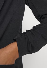 Černý dlouhý rukáv top s nařasením na manžetách a hladkou strukturou, který zdůrazňuje přiléhavý design.