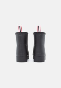 Bottes en caoutchouc noires avec une texture lisse, des semelles plates et des tirettes contrastées rouges et blanches en haut.