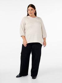 Pullover beige con scollo rotondo e dettagli ricamati sulle spalle. Abbinato a pantaloni neri a gamba larga e calzature nere.