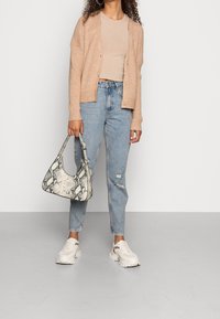 Beige ribbad cardigan, åtsittande beige topp, ljusblå slitna jeans, vita sneakers och en texturerad handväska med ormprint.